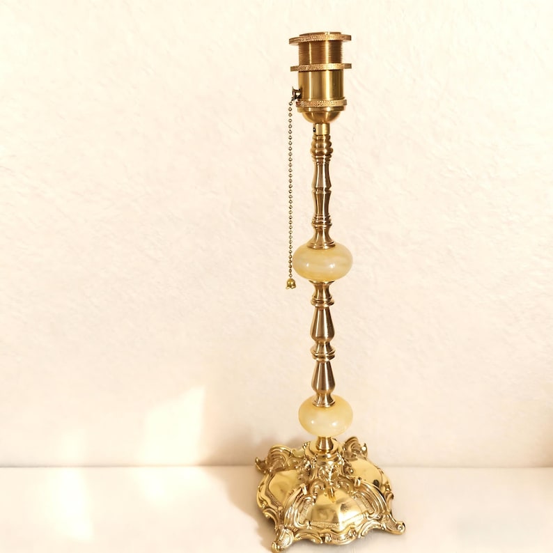 May include: A vintage brass lamp with a decorative base and two cream-colored orbs. The lamp has a pull chain and a detailed, ornate design. The lamp is a classic piece of home decor.