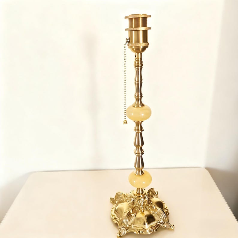 May include: A vintage brass table lamp with a decorative base and two light-colored, orb-shaped accents. The lamp has a pull chain and measures approximately 28 inches tall.