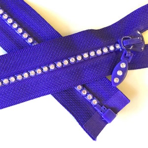 May include: A purple zipper with a row of clear rhinestones along each side. The zipper has a plastic pull with a clear rhinestone design.