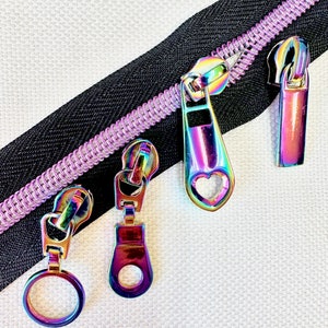 May include: Four iridescent zipper pulls in different styles. The pulls are made of metal and have a rainbow finish. The zipper pulls are on a black and purple zipper tape.