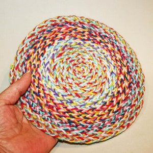 Può includere: Un sottopentola rotondo all'uncinetto colorato con un motivo a spirale in tonalità di rosso, rosa, giallo, blu, verde, bianco e grigio.