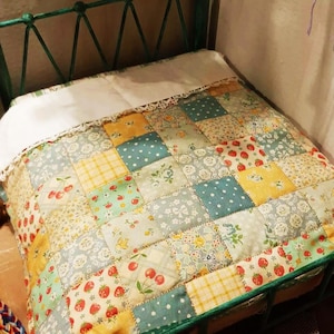 Op de afbeelding: Een groen metalen bedframe met een wit en patchwork dekbed. Het dekbed is gemaakt van verschillende stoffen met bloemen- en geometrische patronen in tinten geel, blauw en rood.