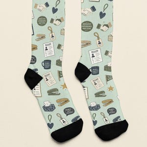 May include: A pair of light green crew socks featuring a repeating office-themed pattern. The design includes illustrations of resumes, staplers, ID badges, tissue boxes, coffee mugs, and handshakes, along with text reading Employee Experience Matters.