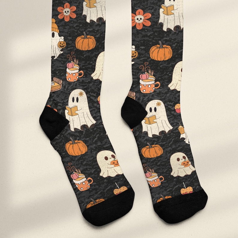 Puede incluir: Un par de calcetines negros con un patr&oacute;n repetitivo de fantasmas blancos, calabazas naranjas, flores naranjas con centros de calavera y tazas naranjas con lunares. Los fantasmas aparecen leyendo libros o sosteniendo calabazas. Tienen talones y punteras negros.