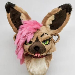 May include: A detailed, plush animal head with large ears, green eyes, and pink faux fur. The head has a brown snout, a red collar, and a pink fringe. The ears are brown and tan. The head is mounted on a stand.