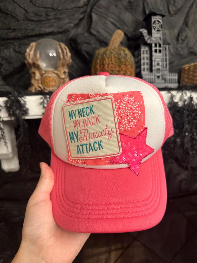 Pu&ograve; includere: Cappellino da camionista rosa con pannello frontale bianco con la scritta "MY NECK MY BACK MY Anxiety ATTACK". &Egrave; attaccata una stella rosa con paillettes. Il cappellino ha una visiera curva e un retro in rete.