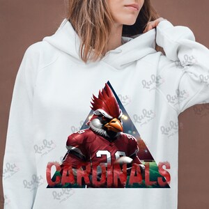 Pu&ograve; includere: Felpa bianca con un mascotte di cardinale rosso che indossa una maglia da calcio con la scritta "CARDINALS" stampata sul davanti. Il mascotte tiene un pallone da calcio.