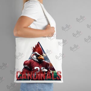 Pu&ograve; includere: Borsa tote bianca con una mascotte di cardinale rosso che indossa una maglia da football con la scritta "CARDINALS" stampata sulla borsa.