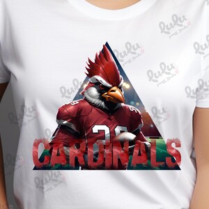 Pu&ograve; includere: Una maglietta bianca con un cardinale rosso che indossa una divisa da football e la parola "CARDINALS" in lettere rosse. Il cardinale &egrave; in un triangolo con uno sfondo sfocato.