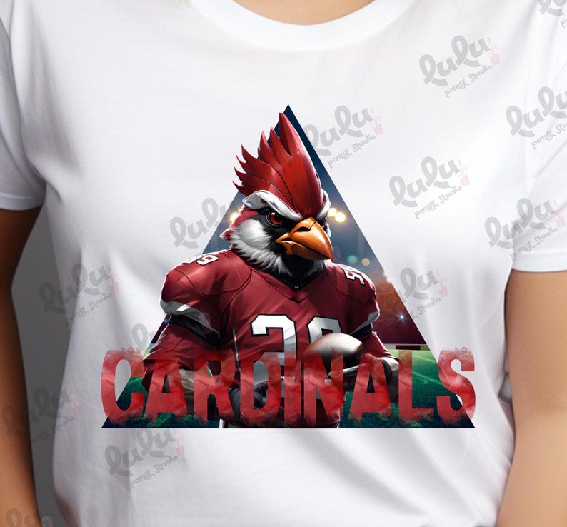 Pu&ograve; includere: Una maglietta bianca con un cardinale rosso che indossa una divisa da football e la parola "CARDINALS" in lettere rosse. Il cardinale &egrave; in un triangolo con uno sfondo sfocato.