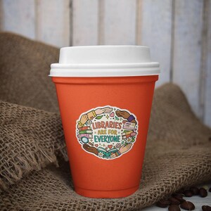 May include: An orange reusable coffee cup with a white lid. The cup has a sticker that reads "LIBRARIES ARE FOR EVERYONE" surrounded by illustrations of books, hands, and flowers. The cup is sitting on a burlap surface with coffee beans scattered around.