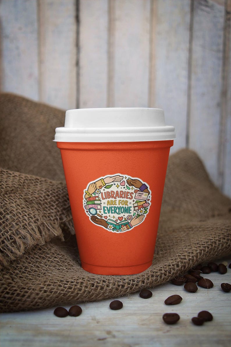 May include: An orange reusable coffee cup with a white lid. The cup has a sticker that reads "LIBRARIES ARE FOR EVERYONE" surrounded by illustrations of books, hands, and flowers. The cup is sitting on a burlap surface with coffee beans scattered around.