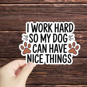 May include: White sticker with black text that reads "I work hard so my dog can have nice things". Two brown paw prints are on either side of the text.