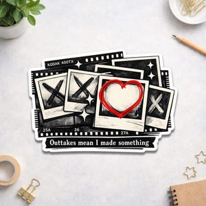 May include: A sticker featuring a collage of black and white film strips and polaroid-style photos. Some photos have an X drawn on them, while one has a red heart. The text "Outtakes mean I made something" is at the bottom.