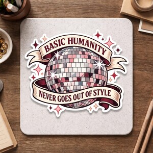 May include: A sticker featuring a disco ball design with the text "BASIC HUMANITY NEVER GOES OUT OF STYLE" on a banner. The disco ball is made of pink, gray, and silver squares, with pink star accents.
