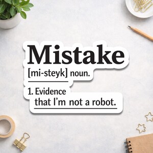 May include: A white sticker with the word "Mistake" in bold black letters. Below, the pronunciation is given as "[mi-steyk] noun." The text continues with "1. Evidence that I'm not a robot."