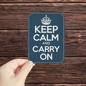 May include: A blue sign with a white crown and the text "Keep Calm and Carry On" on a wood background.