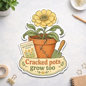 May include: A sticker featuring a yellow flower in a cracked terracotta pot with a packet of wildflower seeds and a small trowel. The text "Cracked pots grow too" is displayed on a banner below the pot.