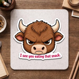 May include: A sticker featuring a cartoon bull with an angry expression. The bull is brown with white horns and a pink nose. The text "I see you eating that snack" is below the bull.