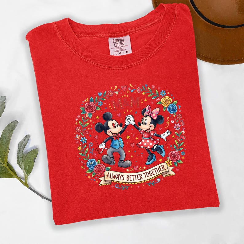 Puede incluir: Camiseta roja con un dise&ntilde;o de Mickey y Minnie Mouse tomados de la mano, rodeados por una corona floral. El texto "ALWAYS BETTER TOGETHER" est&aacute; en una pancarta. La camiseta est&aacute; hecha de un material suave.