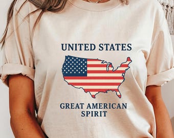 May include: A beige t-shirt featuring a graphic of the United States map in red, white, and blue, resembling the American flag. The text "UNITED STATES" is above the map, and "GREAT AMERICAN SPIRIT" is below.