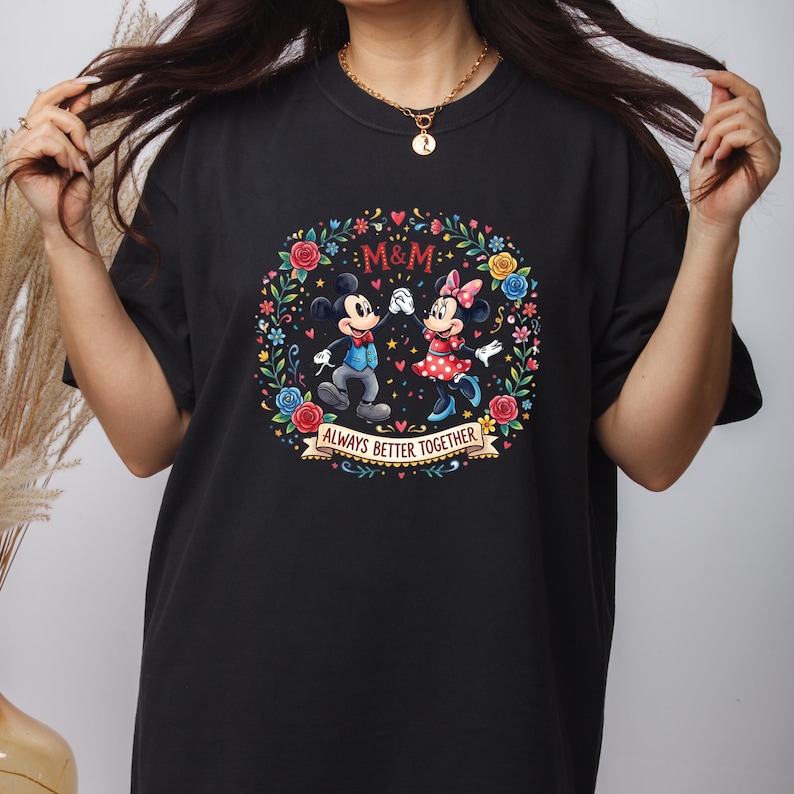 Puede incluir: Camiseta negra con un dise&ntilde;o de corona floral colorida con Mickey y Minnie Mouse. El dise&ntilde;o incluye el texto "M&M" y "Always Better Together" en una pancarta. La camiseta es de cuello redondo.