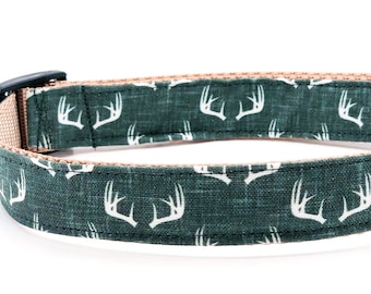 May include: A green dog collar with a white antler pattern. The collar has a black buckle and a silver D-ring.