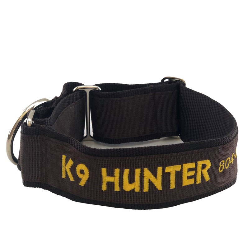 May include: A dark brown nylon dog collar featuring the embroidered yellow text K9 HUNTER and the partial number 804. The collar includes a silver-toned metal D-ring for leash attachment and a sliding metal adjuster for sizing the strap.