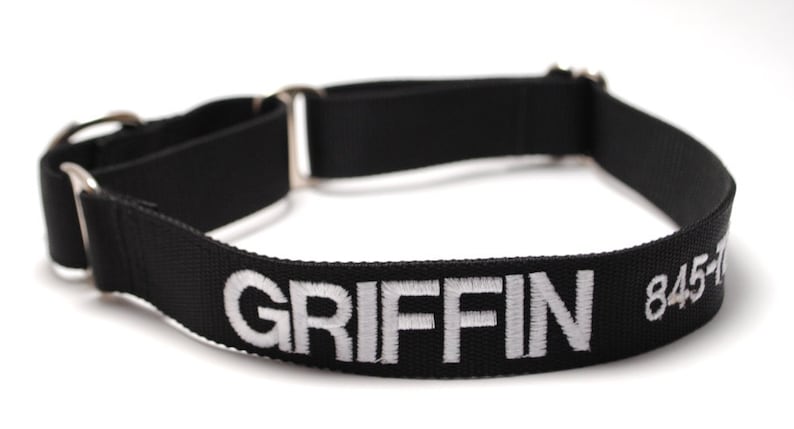 May include: Black dog collar with the name "GRIFFIN" embroidered in white. The collar also has a phone number embroidered in white. The collar is made of a durable black material and features silver-colored metal hardware.