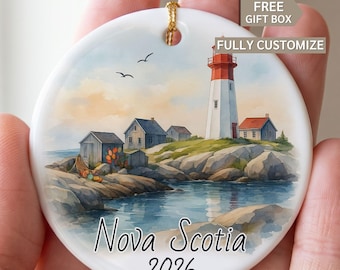 May include: A round white ceramic ornament featuring a watercolor illustration of a lighthouse, small coastal houses, and rocky terrain by the water. The text "Nova Scotia" and "2026" is printed at the bottom. Includes text "FREE GIFT BOX" and "FULLY CUSTOMIZE".