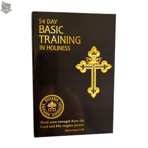 Puede incluir: Un libro negro con letras doradas que dice "54 Day Basic Training in Holiness". Un diseño de cruz y corona dorada está en el lado derecho. El libro también presenta el texto "Draw your strength from the Lord and His mighty power. Ephesians 6.10."