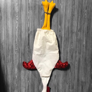 Puede incluir: Un pollo de tela blanca con alas rojas y patas amarillas colgando boca abajo. El pollo est&aacute; hecho de tela y tiene un patr&oacute;n de lunares blancos.