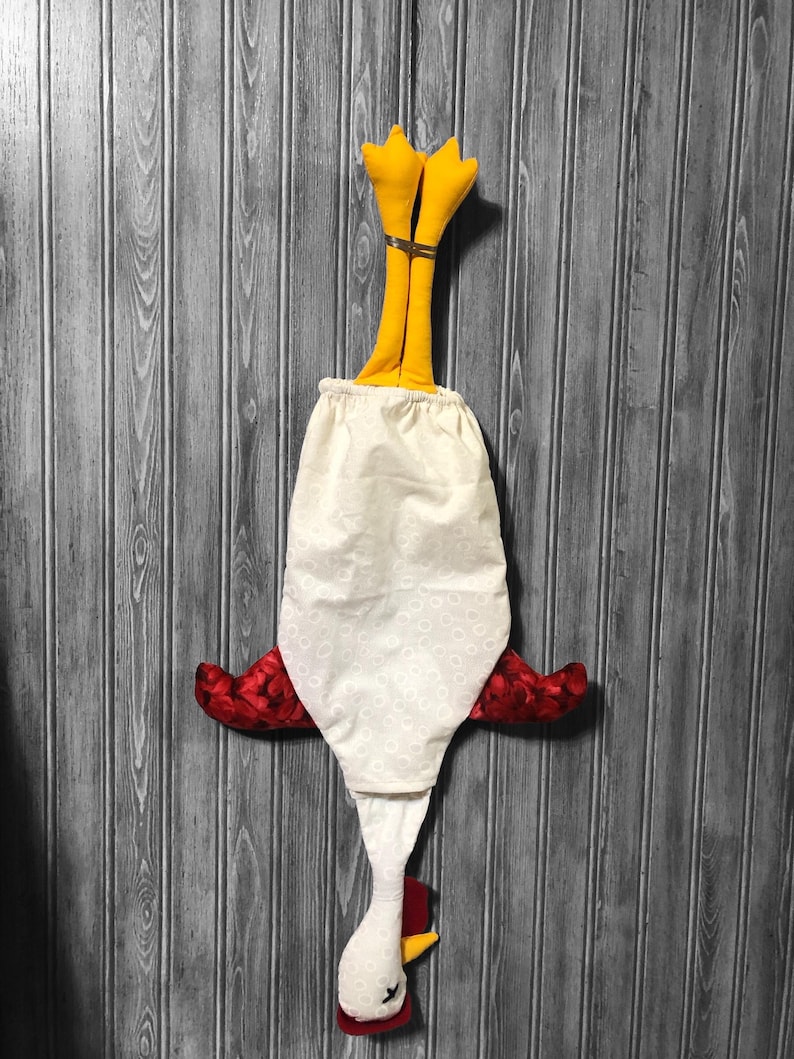 Puede incluir: Un pollo de tela blanca con alas rojas y patas amarillas colgando boca abajo. El pollo est&aacute; hecho de tela y tiene un patr&oacute;n de lunares blancos.
