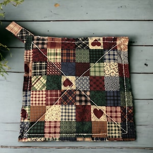 May include: A patchwork pot holder with a red, green, blue, and yellow color scheme. The pot holder has a loop handle and is made of fabric with a quilted design.