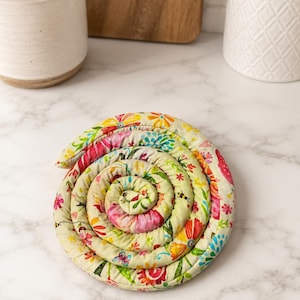 May include: A spiral-shaped, floral-patterned trivet. The trivet features a cream-colored background with a vibrant array of flowers in shades of red, pink, yellow, and blue. The trivet is designed to protect surfaces from hot items.