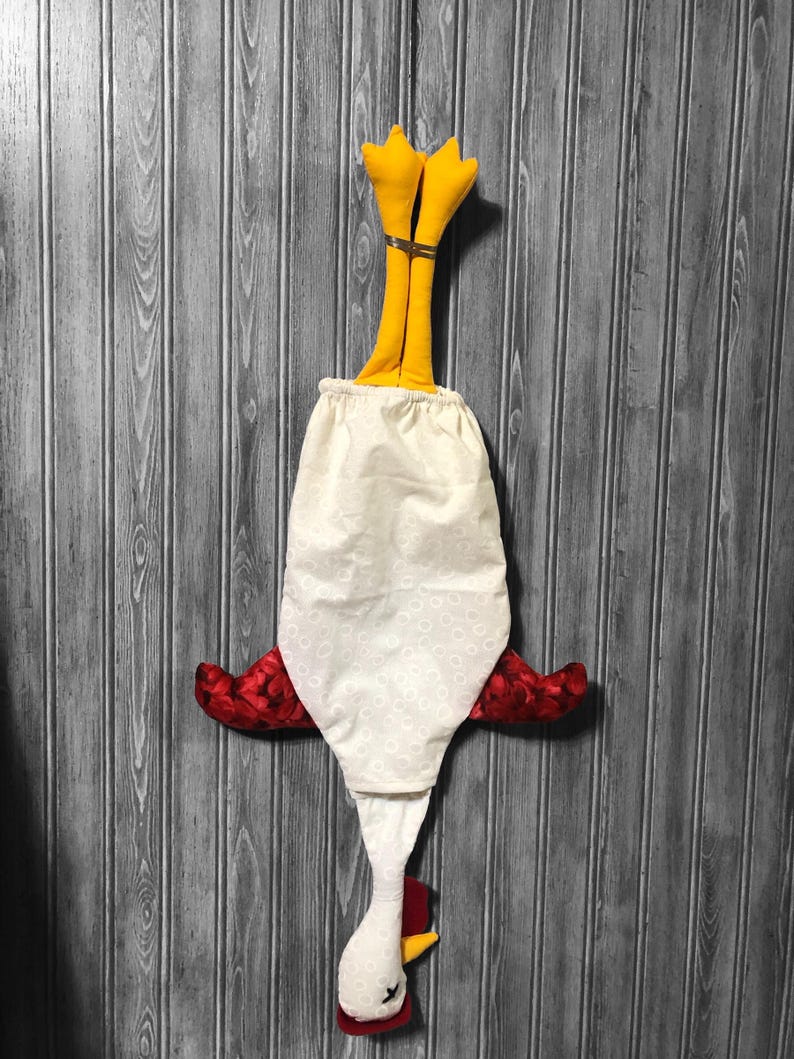 Puede incluir: Un pollo de tela blanca con alas rojas y patas amarillas colgando boca abajo. El pollo est&aacute; hecho de tela y tiene un patr&oacute;n de lunares blancos.