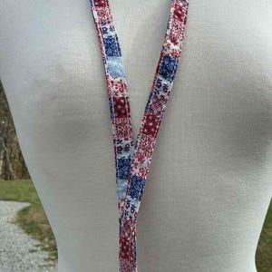 May include: A patterned lanyard with red, white, and blue squares. The lanyard is made of fabric and has a silver-colored metal clasp at the bottom. The background is a blurred outdoor scene.