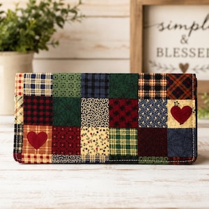 May include: A patchwork wallet with a variety of fabric patterns in red, green, blue, and yellow. Two red heart appliqués are visible on the front. The wallet is rectangular and appears to be made of quilted fabric.