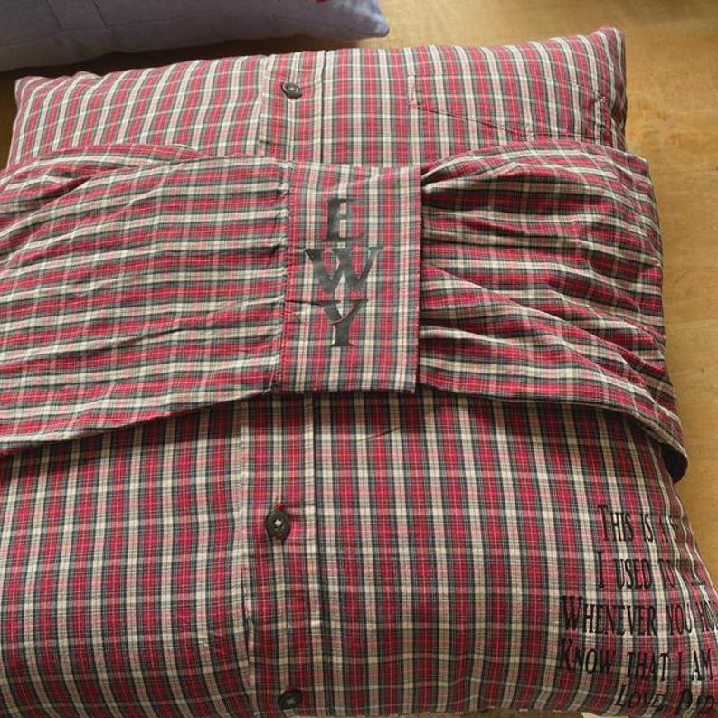 Pode incluir: Travesseiro xadrez vermelho e preto com um bot&atilde;o branco e as letras "EWY" bordadas na frente. O travesseiro tem uma cita&ccedil;&atilde;o nas costas que diz "Isso &eacute; algo que eu costumava dizer sempre que voc&ecirc; sabia que eu estava prestes a morrer."