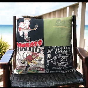 May include: A square pillow with a patchwork design featuring sports and vintage-themed graphics. The pillow has a hockey player, baseball player, and a vintage liquor label. The pillow is on a wooden chair.