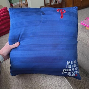 May include: Blue pillow made from a shirt. The pillow has a buttoned collar and a red "P" logo. Text on the pillow reads "This is a shirt I used to wear...Love Nick."