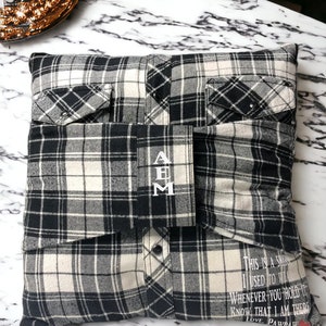 Pode incluir: Uma almofada de xadrez preto e branco com um bolso de cada lado. A almofada tem as iniciais "A B M" bordadas na frente. A parte de tr&aacute;s da almofada tem o texto "This is a shirt I used to wear. Whenever you hold it know that I am there. Love, Pawdaw" impresso nela.