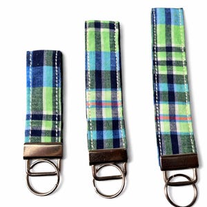 May include: Three fabric key fobs in varying lengths. Each fob features a blue, green, and white plaid pattern with a metal clasp and key ring. The fobs are stitched with white thread.