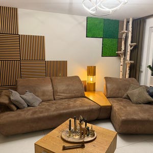 Könnte beinhalten: Ein braunes Ledersofa mit zwei Kissen, ein Holz-Couchtisch mit Dekoartikeln und eine Stehlampe mit goldener Basis und weißem Schirm. Die Wand hinter dem Sofa ist mit Holzpaneelen und einer grünen Mooswandkunst dekoriert.