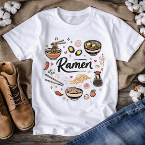 Könnte beinhalten: Weißes T-Shirt mit einer farbenfrohen Illustration von Ramen-Schalen, Nudeln, Eiern und anderen Zutaten. Das Wort "Ramen" ist in einer stilvollen Schriftart geschrieben. Das Design umfasst Essstäbchen, Chilischoten und eine Sojasoßenflasche.