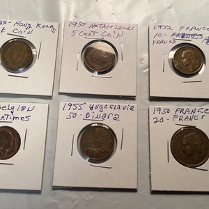 May include: A collection of vintage coins from various countries, including Hong Kong, Netherlands, France, Belgium, and Yugoslavia. Each coin is displayed in a protective holder with handwritten details of the year and denomination.