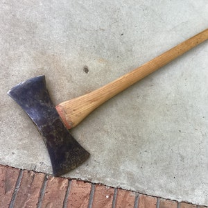 May include: A double-headed axe with a wooden handle. The axe head is made of metal and has a dull finish. The handle is made of wood and has a natural finish.