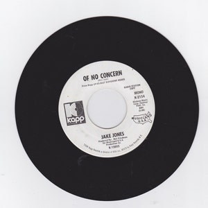 May include: A vintage 45 RPM vinyl record with a black outer edge and a white center label. The label features the text "OF NO CONCERN" by Jake Jones, along with the Kapp Records logo and other details. The record is a mono copy.
