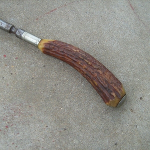 May include: A vintage, metal and antler handled tool with a silver band. The tool has a brown antler handle with a silver cap.
