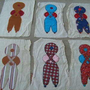 May include: Six handmade fabric doll figures on white fabric squares. The dolls are made of different colored fabrics and have different patterns. The dolls are all wearing different colored clothes.